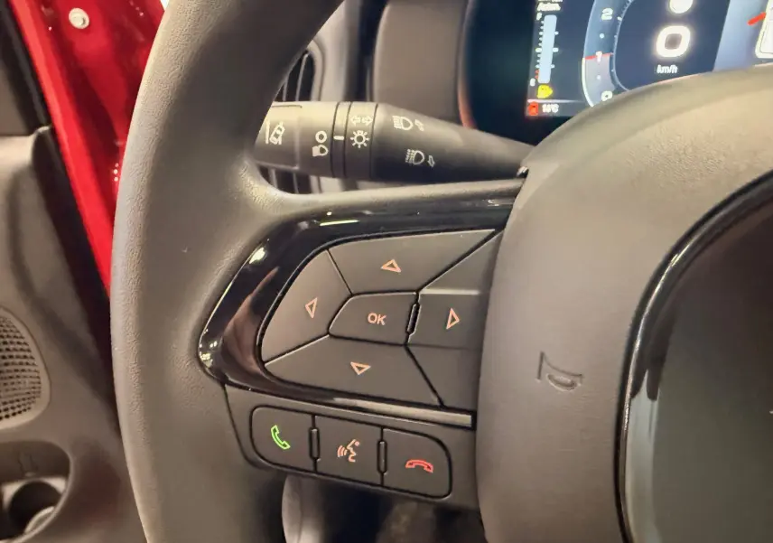 Gros plan sur le volant de la Fiat Panda 2025 Rouge Amore, avec commandes multifonctions et tableau de bord numérique partiel.