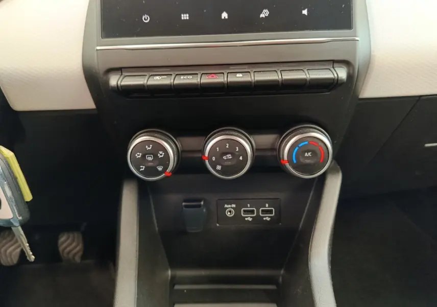 Vue rapprochée du tableau de bord central de la Renault Clio blanc, montrant les commandes de climatisation et ports USB.