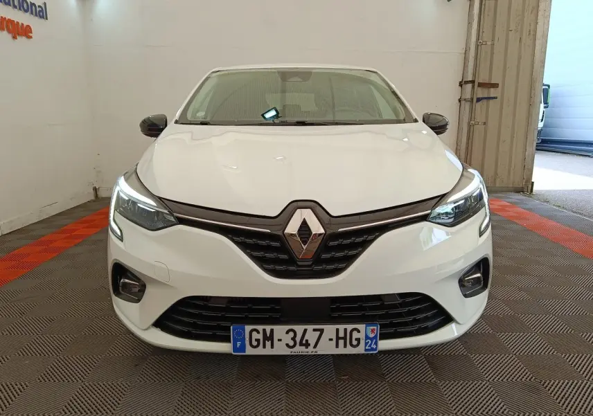 Vue de face d'une Renault Clio Evolution TCe 100 GPL blanche avec phares LED allumés dans un garage.