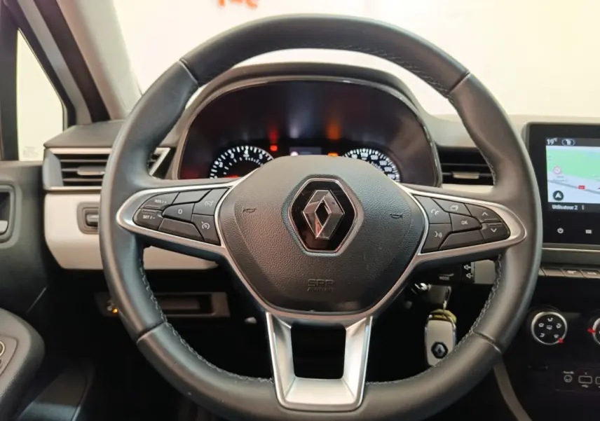 Vue rapprochée du volant cuir noir de la Renault Clio 2023 avec commandes multifonctions et tableau de bord éclairé.