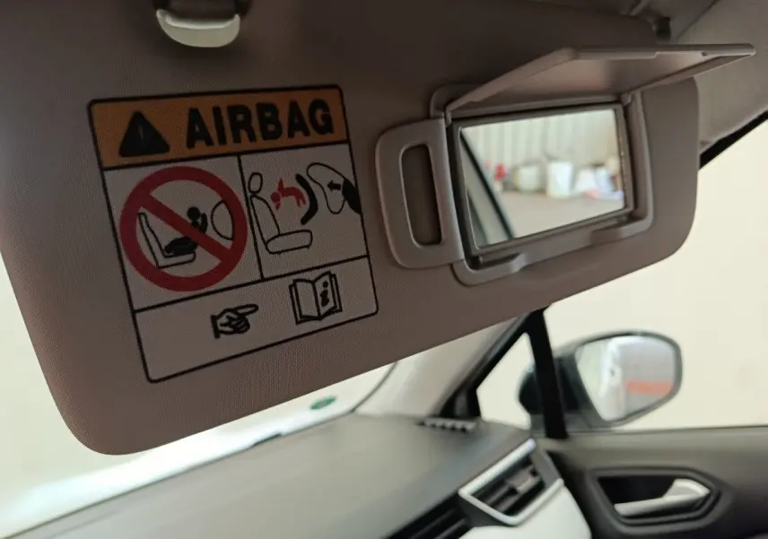 Détail intérieur de la Renault Clio blanc, miroir de pare-soleil côté conducteur avec avertissement airbag visible.
