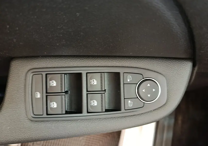 Gros plan sur les commandes des vitres électriques et rétroviseurs du côté conducteur d’une Renault Clio blanche Evolution TCe 100 GPL.