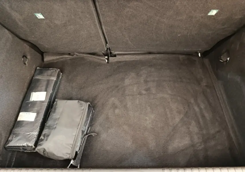 Coffre vide de Renault Clio blanc, vue intérieure montrant la moquette noire et deux sacs de rangement.