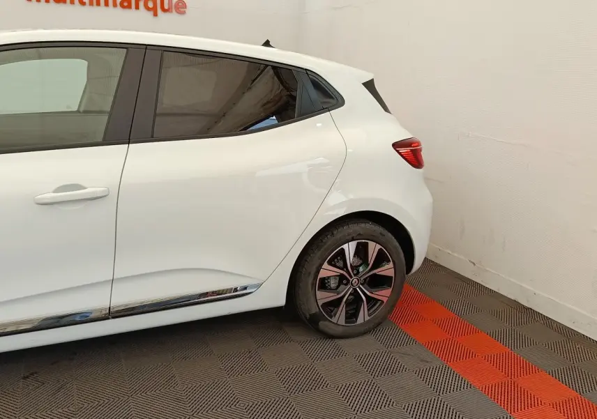 Vue latérale droite sur l'arrière d'une Renault Clio blanche 2023 avec jante alliage et poignée de porte intégrée.
