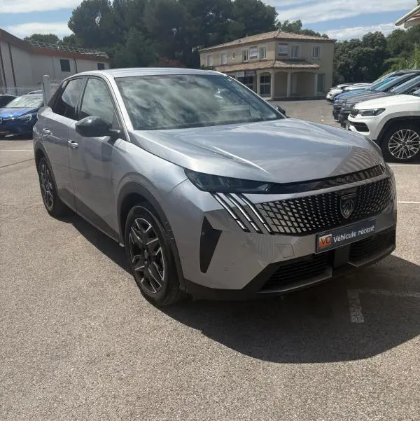 Peugeot 3008 Hybrid gris clair en 3/4 avant droit, avec calandre distinctive et phares LED fins, stationné en extérieur.