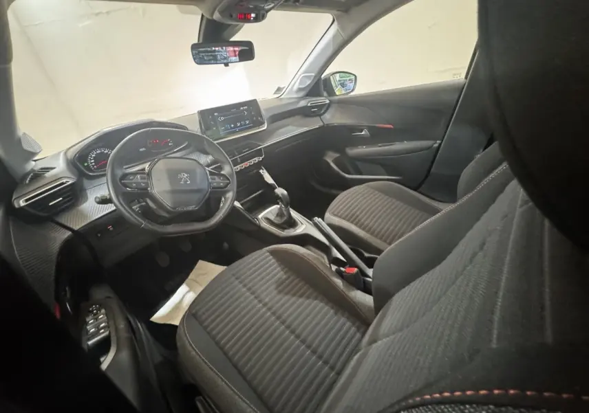 Vue intérieure côté conducteur de la Peugeot 208 PureTech 75 S&S Active Pack avec tableau de bord noir et volant cuir.