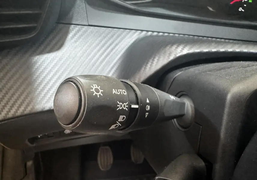 Gros plan sur la manette de commande des phares à gauche du volant dans l’habitacle de la Peugeot 208 jaune.