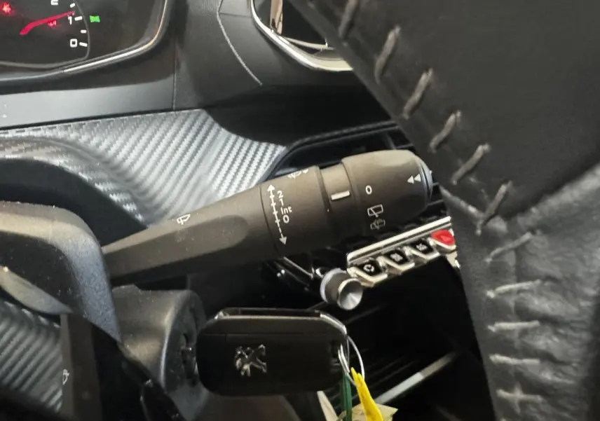 Gros plan intérieur sur la colonne de direction et clé Peugeot, volant cuir avec surpiqûres visibles.
