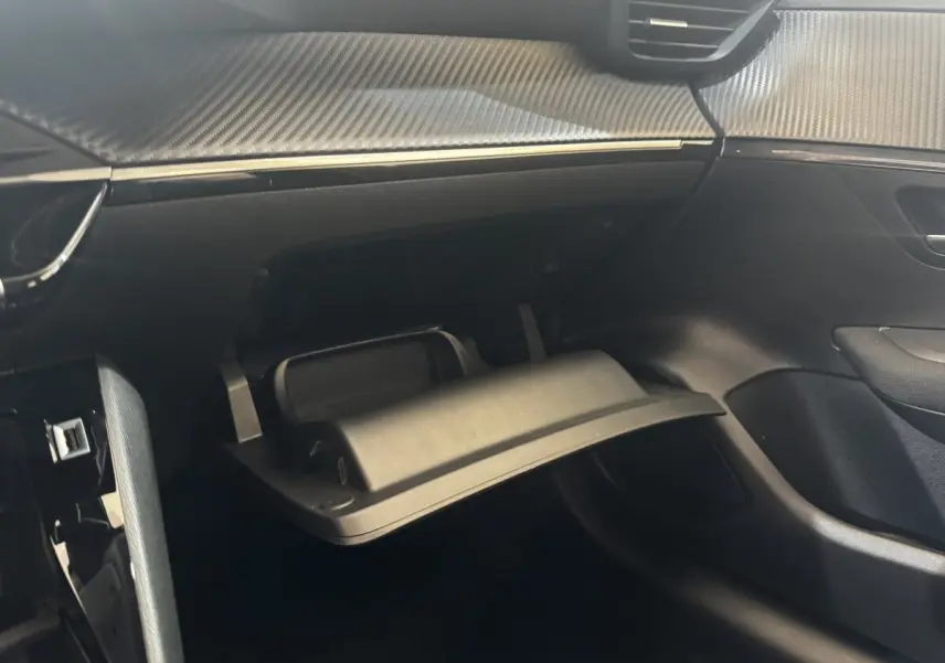 Vue intérieure côté passager de la Peugeot 208 jaune 2023, avec boîte à gants ouverte et tableau de bord noir.