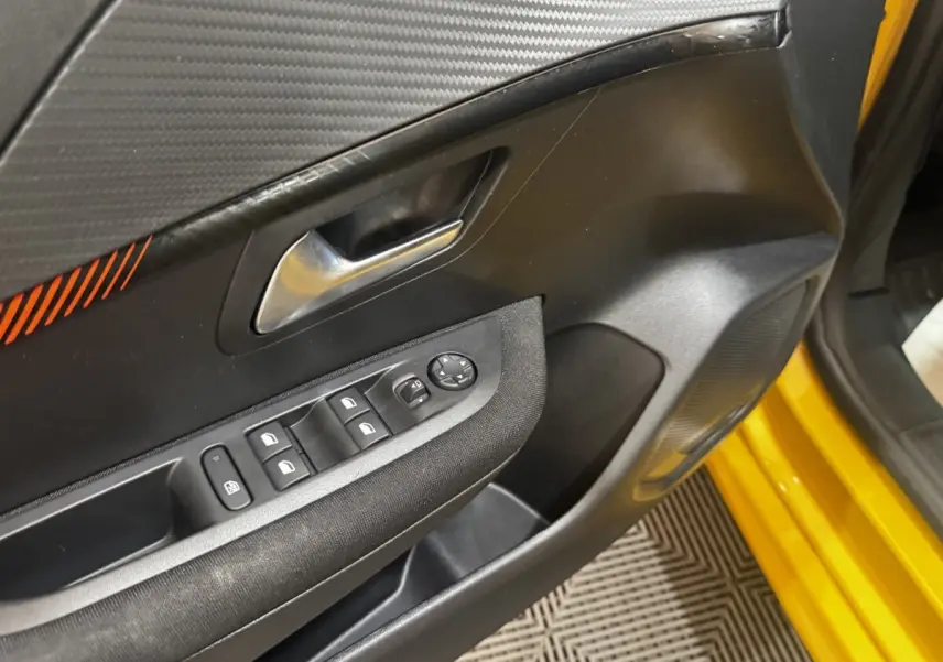 Vue rapprochée de la porte avant gauche jaune de la Peugeot 208 avec commandes des vitres et rétroviseurs.