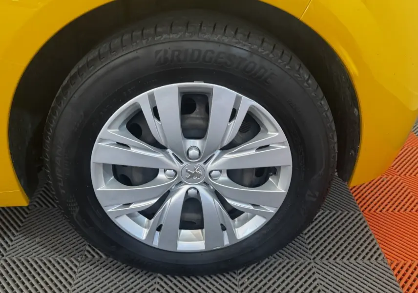 Gros plan sur la roue avant gauche d’une Peugeot 208 jaune 2023 avec jante argentée et pneu Bridgestone.