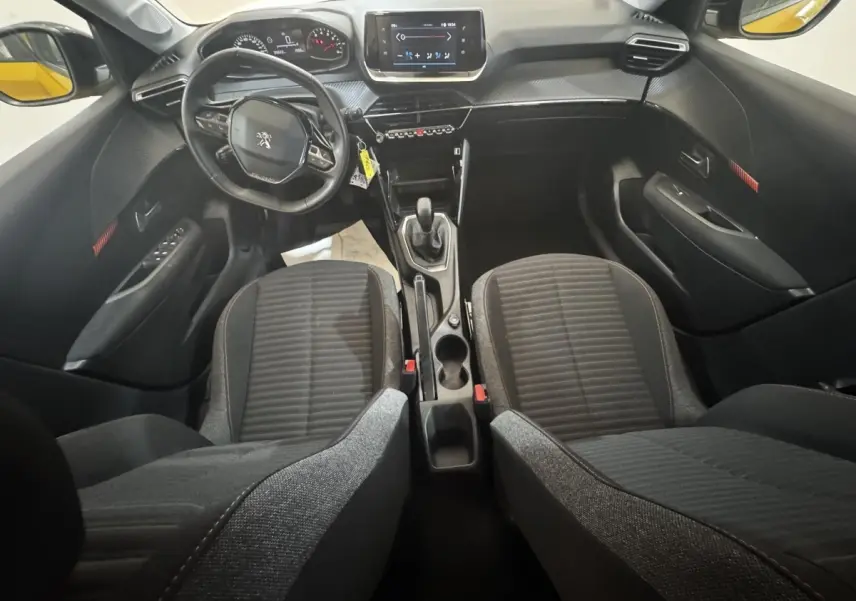 Vue intérieure avant de la Peugeot 208 jaune 2023, montrant le volant cuir, tableau de bord et écran tactile central.
