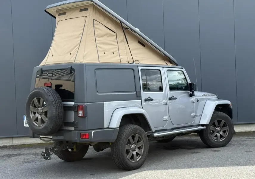 Jeep Wrangler 2.8 CRD 2019 Billet Silver vue 3/4 arrière avec toit relevable beige et cellule de vie intégrée.