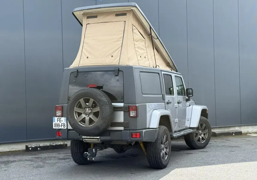 Vue 3/4 arrière droite du Jeep Wrangler Billet Silver avec toit relevable beige et roue de secours sur hayon.