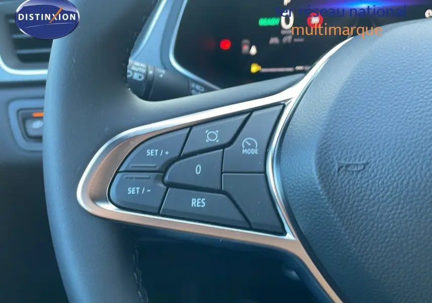 Gros plan sur les commandes à gauche du volant du Renault Captur blanc nacré 2025 avec tableau de bord numérique en arrière-plan.