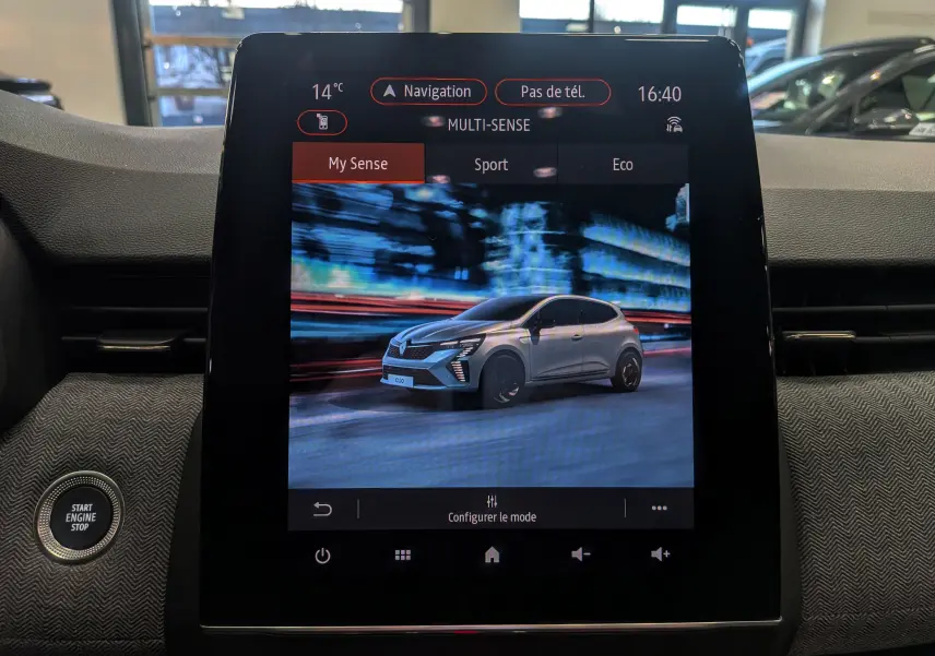 Écran central montrant une Renault Clio V grise en 3/4 avant dans un décor urbain nocturne flouté.