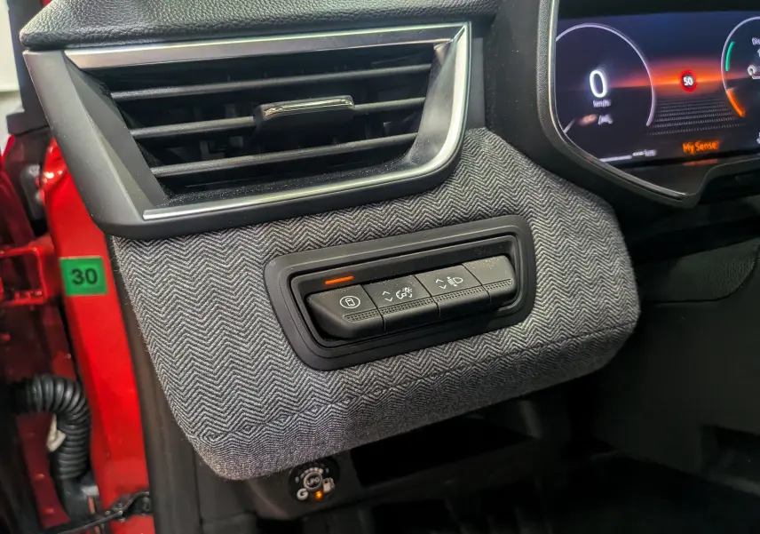 Détail intérieur côté gauche montrant la commande des feux et la texture tissu chevrons gris sur Renault Clio V Rouge Flamme.