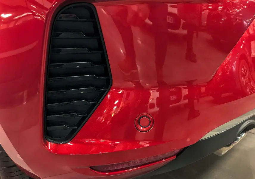 Détail du pare-chocs arrière droit rouge flamme de la Renault Clio V ECO-100 CH TECHNO avec capteur de recul et diffuseur noir.
