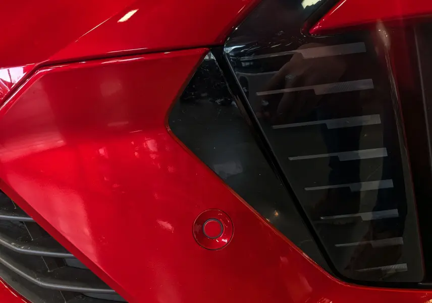 Gros plan sur le feu arrière droit noir et la carrosserie rouge flamme d'une Renault Clio V ECO-100 CH TECHNO 2025.