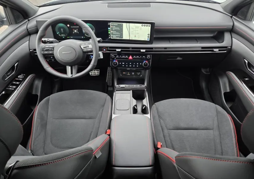 Vue intérieure avant du Hyundai Tucson 2025 N Line, sellerie cuir/alcantara noire avec surpiqûres rouges et écran tactile 12,3 pouces.
