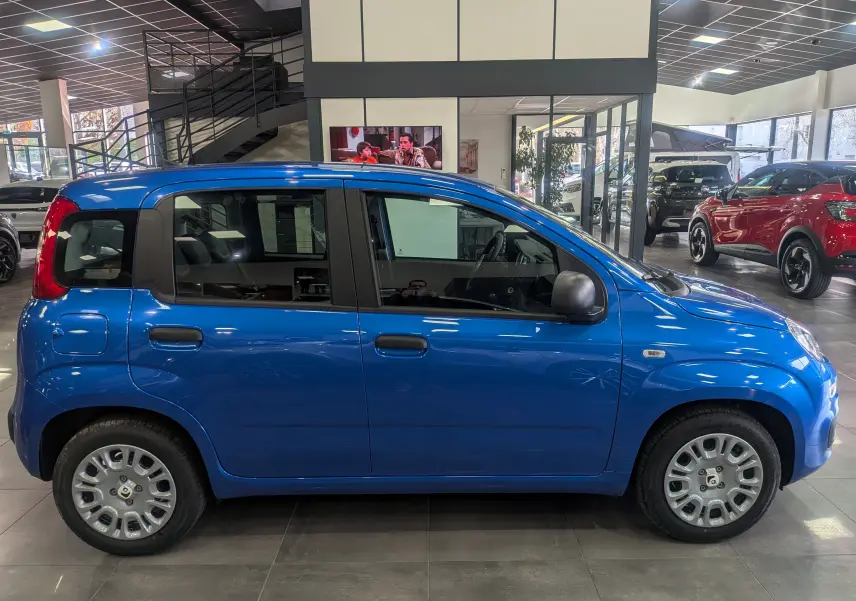 Vue de profil côté gauche d'une Fiat Panda 1.0 Hybrid City 2025 en Bleu Italia dans un showroom lumineux.
