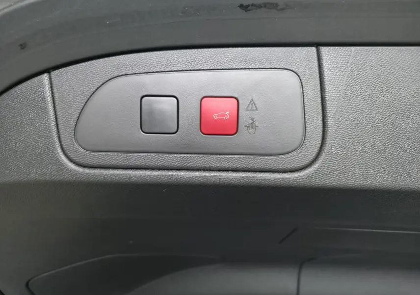 Gros plan sur les boutons du hayon motorisé, dont un rouge avec pictogramme de coffre, intérieur noir.