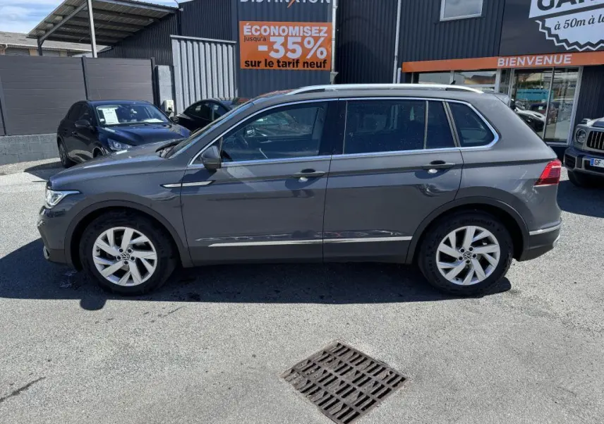 Profil côté gauche d'un Volkswagen Tiguan gris 2021 garé devant un garage avec jantes alliage 18 pouces.