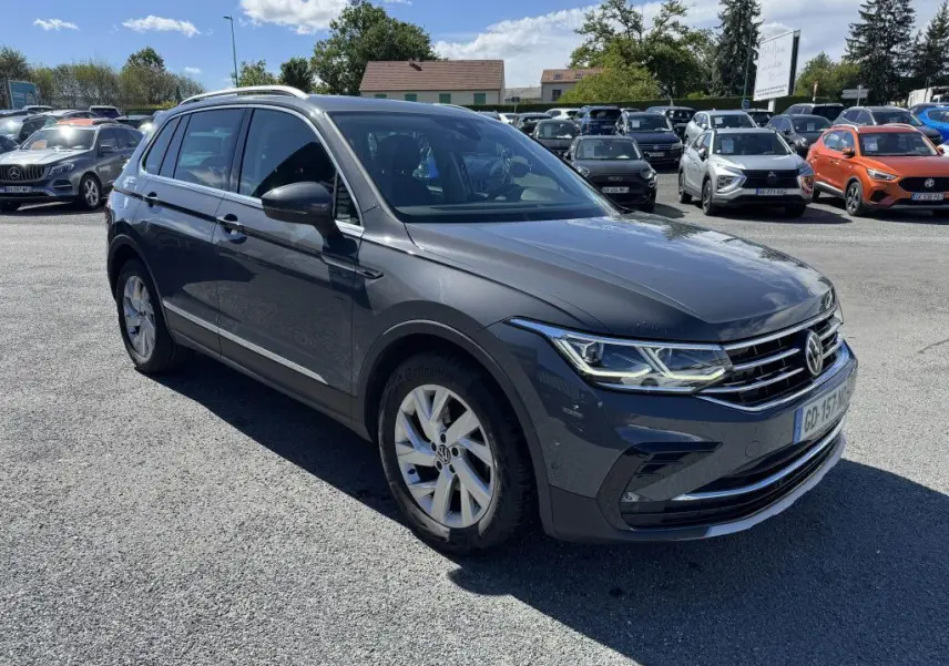 Volkswagen Tiguan gris 3/4 avant droit, avec jantes alliage et calandre chromée, stationné en extérieur.