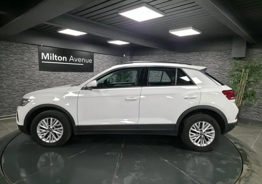 Profil côté gauche d'un Volkswagen T-Roc blanc 2022 avec jantes alliage et toit noir en showroom.