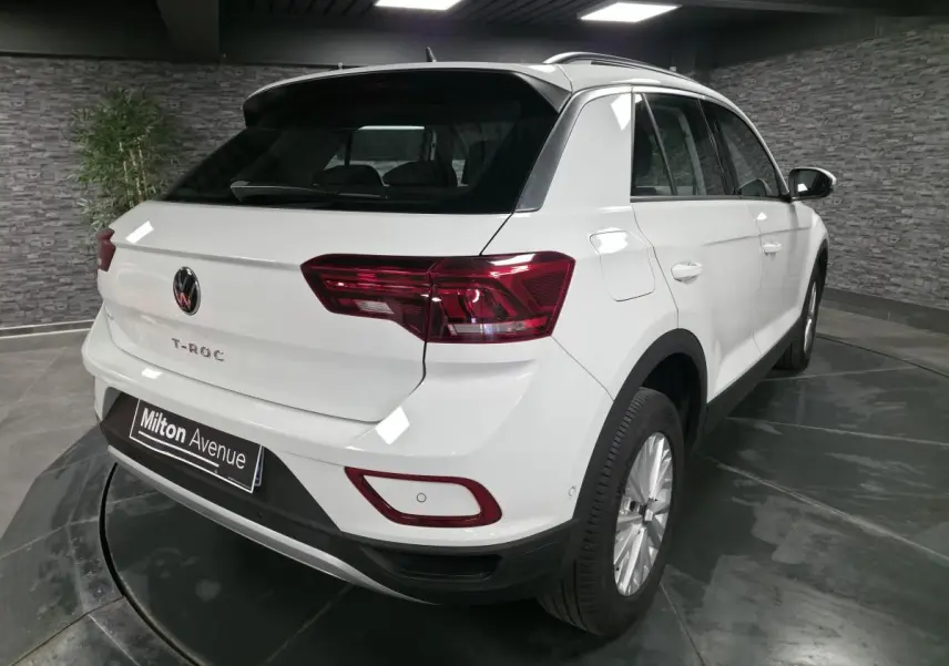 Vue 3/4 arrière droite d'un Volkswagen T-Roc blanc avec feux arrière LED et jantes alliage 16 pouces dans un showroom.