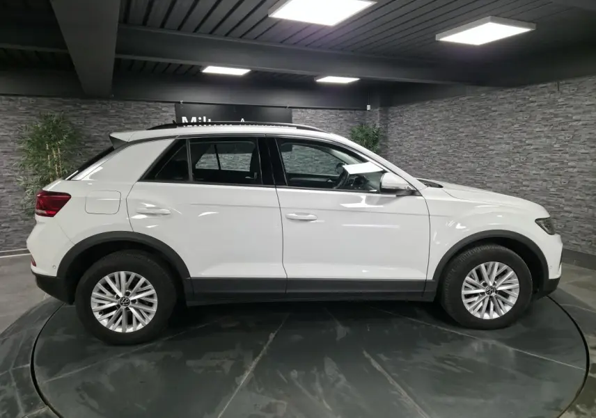Volkswagen T-Roc blanc vu de profil côté gauche, avec jantes alliage 16 pouces et toit noir contrasté.