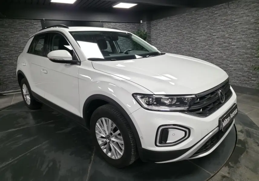 Volkswagen T-Roc blanc vue 3/4 avant droit en intérieur avec jantes alliage et feux LED circulaires.