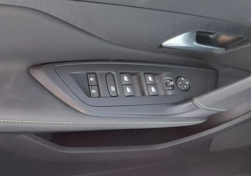 Détail de la porte côté conducteur de la Peugeot 308 Hybrid gris, avec commandes électriques et surpiqûres vertes.