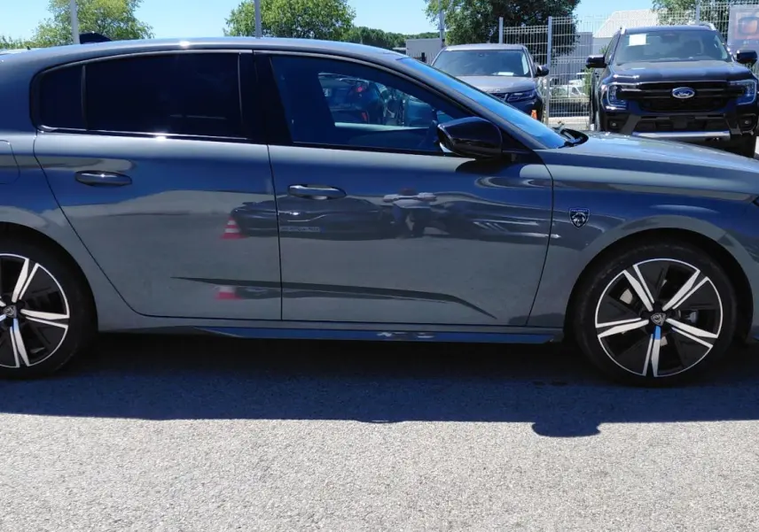 Profil côté gauche d'une Peugeot 308 Hybrid 145 e-DCS6 GT gris avec jantes alliage 18 pouces sur parking extérieur.