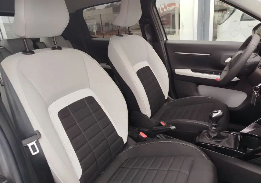 Vue intérieure côté avant droit de la Citroën C3 1.2 Turbo 2025, sièges bicolores gris clair et noir avec boîte manuelle.