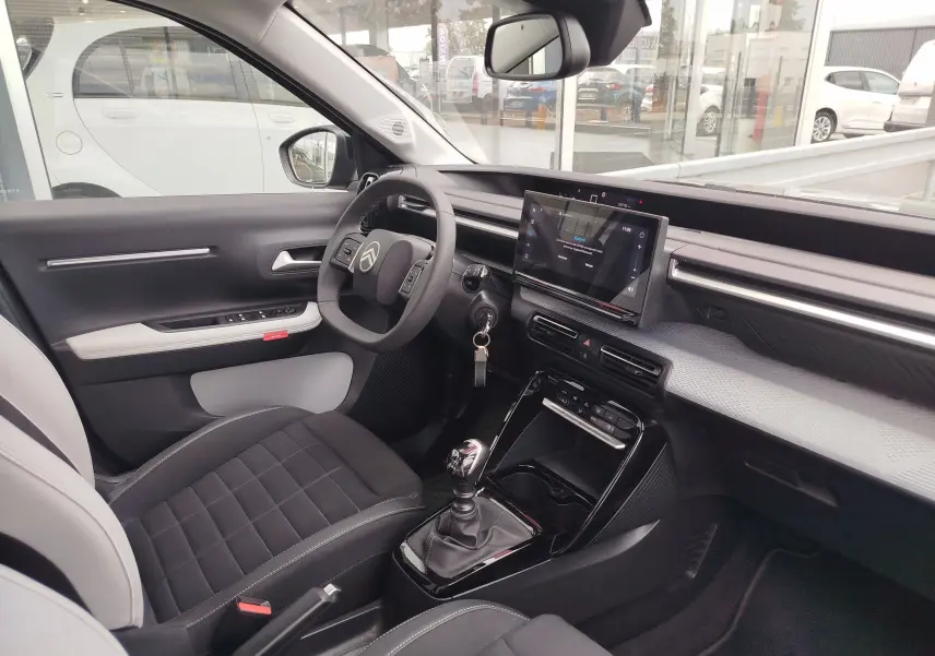 Intérieur avant droit de la Citroën C3 2025 gris foncé, volant multifonction, écran tactile et boîte manuelle visible.