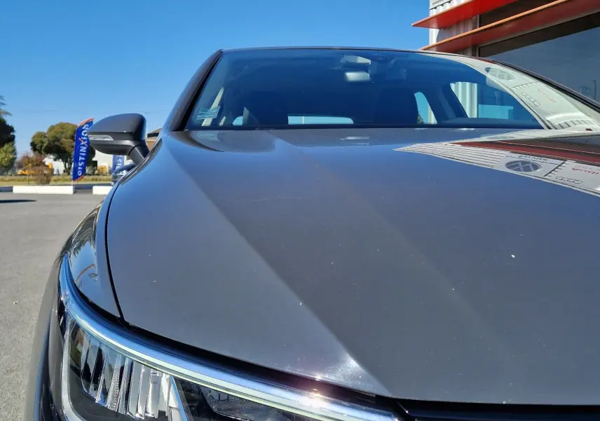 Gros plan sur l'avant gauche d'une Volkswagen Golf A8 gris Urano, mettant en valeur le phare et la calandre sous un ciel bleu.