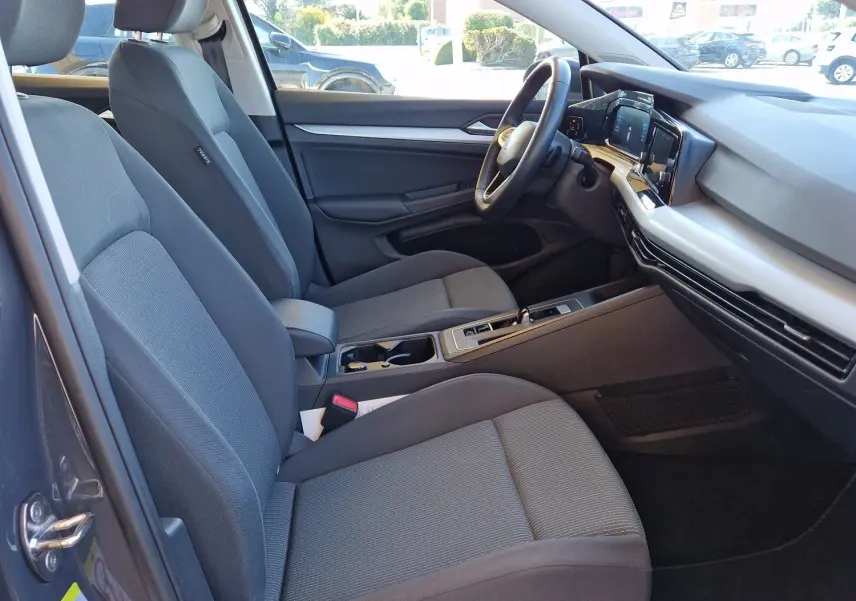 Vue intérieure côté conducteur de la Volkswagen Golf A8 2023 gris Urano, montrant sièges tissu et tableau de bord moderne.