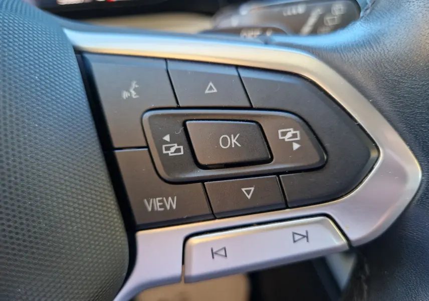 Gros plan sur les commandes multifonctions noires et argentées du volant côté gauche d'une Volkswagen Golf gris Urano 2023.