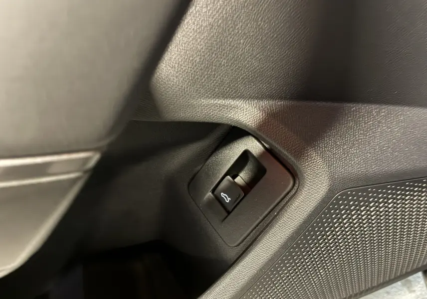 Bouton d'ouverture du coffre en plastique noir sur le panneau intérieur côté gauche d'un CUPRA Formentor gris foncé.