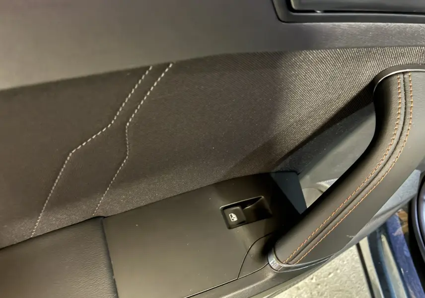 Gros plan sur la poignée intérieure en cuir noir avec surpiqûres marron et bouton de lève-vitre du côté gauche d'une CUPRA Formentor 2024.