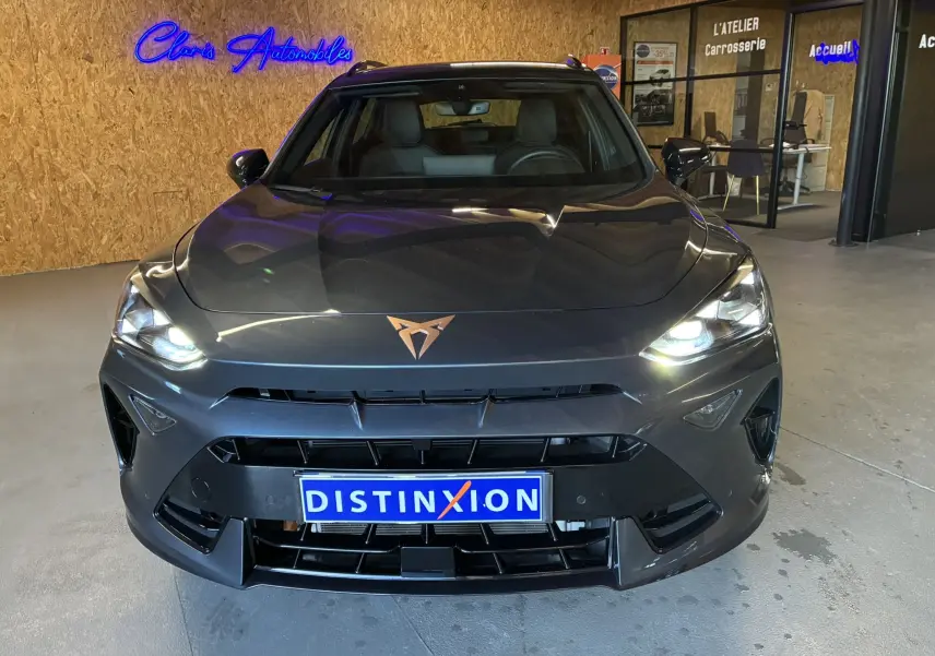 Vue frontale d'un CUPRA Formentor gris foncé 2024 avec phares allumés et logo cuivre, en intérieur showroom.