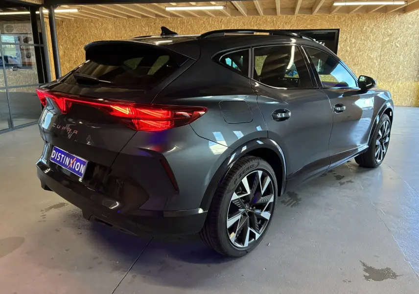 Vue 3/4 arrière droite d'une CUPRA Formentor gris foncé avec feux arrière allumés et jantes bi-ton 19 pouces.