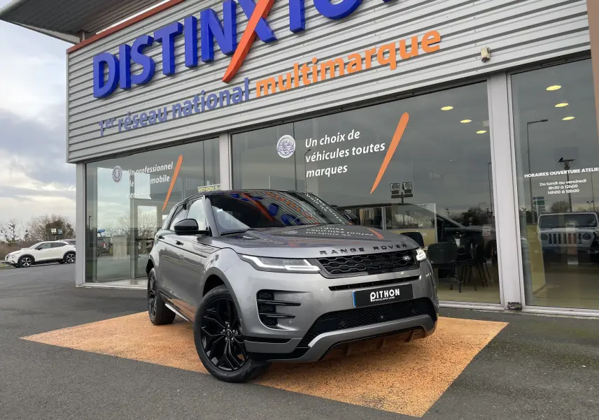 Vue 3/4 avant d'un Range Rover Evoque 200D SE R-Dynamic gris Eiger avec jantes noires, devant un showroom multimarque.