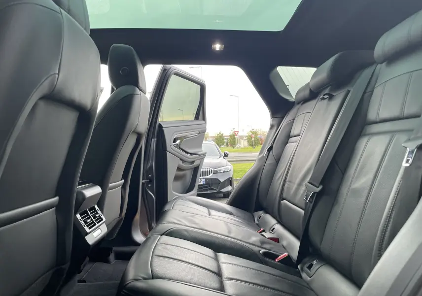 Vue intérieure arrière du Range Rover Evoque 200D SE R-Dynamic en cuir noir, avec porte arrière gauche ouverte et toit panoramique.