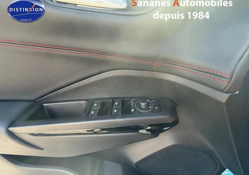 Gros plan sur la porte côté conducteur du Ford Puma bleu, montrant les commandes des vitres et rétroviseurs avec surpiqûres rouges.