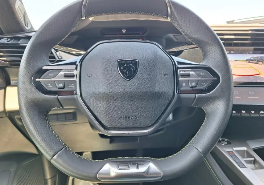 Vue rapprochée du volant cuir noir de la Peugeot 308 Hybrid 145 e-DCS6 GT avec logo et badge GT visible.