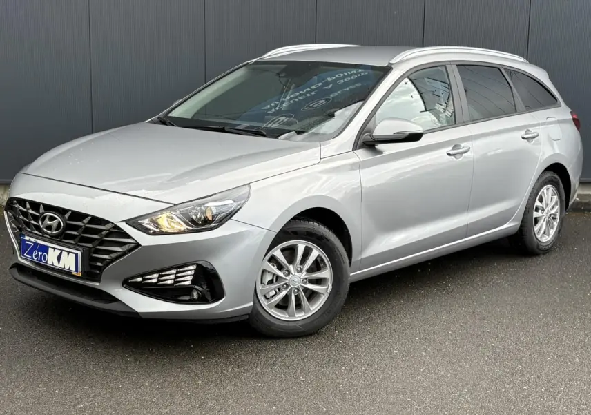 Hyundai i30 SW T-GDI 120 Modern gris argent en 3/4 avant droit, avec jantes alliage et feux allumés.