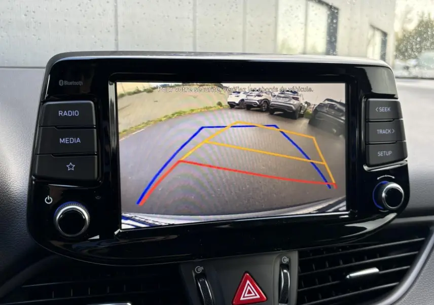 Écran tactile central affichant la caméra de recul avec lignes de guidage dans une Hyundai i30 SW T-GDI 120 Modern gris argent.
