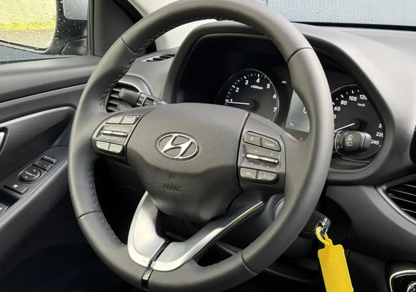 Vue rapprochée du volant cuir noir de la Hyundai i30 SW T-GDI 120 Modern 2025 avec commandes intégrées et tableau de bord visible.